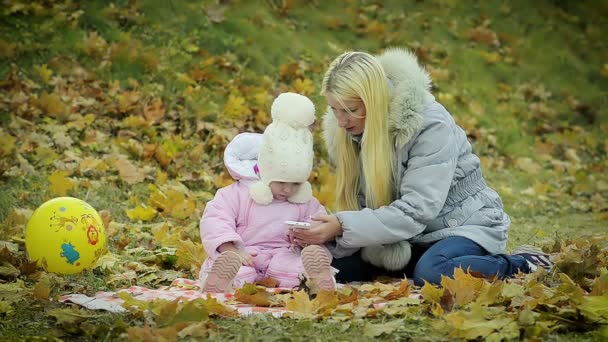 Мама с маленькой дочкой смотрят фото на телефон в парке — стоковое видео