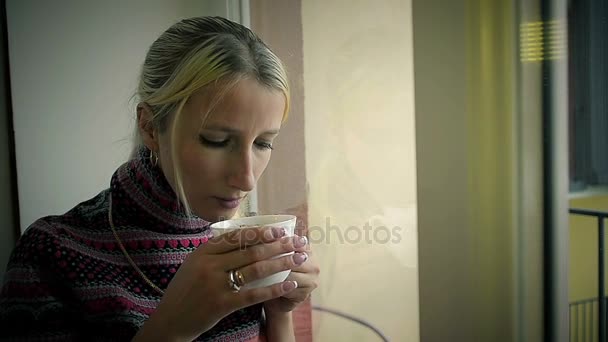 Nahaufnahme trauriges Mädchen, das zu Hause Kaffee trinkt und aus dem Fenster schaut — Stockvideo