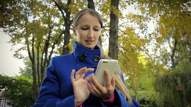 Happy Girl se comunica en las redes sociales en el teléfono inteligente en un parque — Vídeo de stock