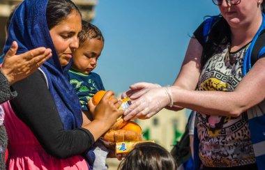 Suriye kadın küçük oğlu ile Yunan limanda bir mülteci kampında hayırsever kuruluşlardan suyu ve meyve almak