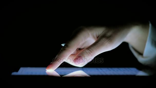 Gros plan de la main féminine sur l'écran de la tablette dans l'obscurité 