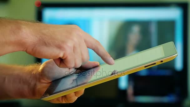 Primer plano de las manos masculinas usando una tableta en casa en el fondo de la TV — Vídeo de stock