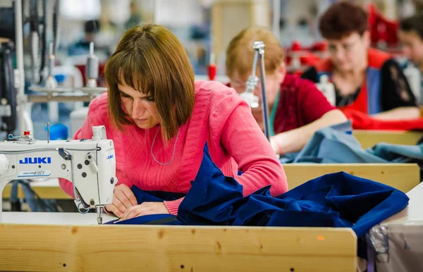 Jovem costureira costura em ambiente de fábrica de vestuário — Fotografia de Stock