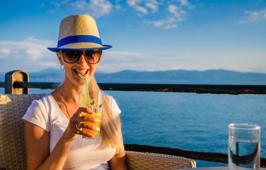 Taze deniz kenarında bir kafede bir genç mutlu kız içme turuncu yakın çekim