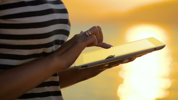 Close-up girl utiliza una tableta para comunicarse en las redes sociales en un viaje por el mar en la puesta del sol . — Vídeos de Stock