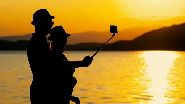 Silueta pareja tomando fotos móviles selfie en un viaje por el mar en la puesta del sol . — Vídeo de stock