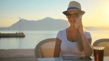 Sunset bulvarında bir gezi denizin kenarında akıllı telefon konuşurken şapkalı genç kız.