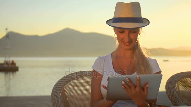 Zbliżenie dziewczyna komunikuje się w sieciach społecznościowych na tablecie w letniej kawiarni na zachód słońca. — Wideo stockowe