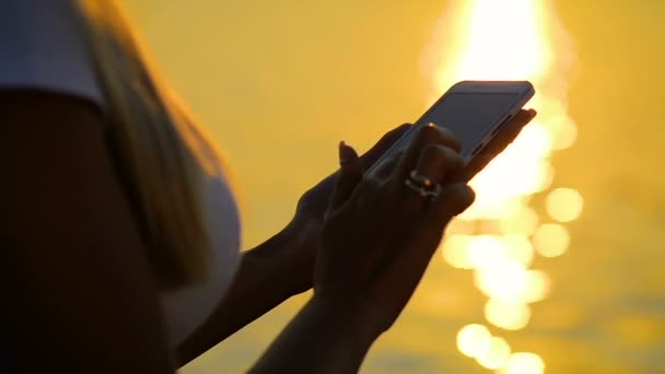 Närbild flicka använder smartphone på en resa av havet på solnedgången. — Stockvideo