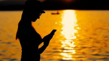 Sunset bulvarında bir gezi denizin kenarında Smartphone kullanan bir kız siluet.