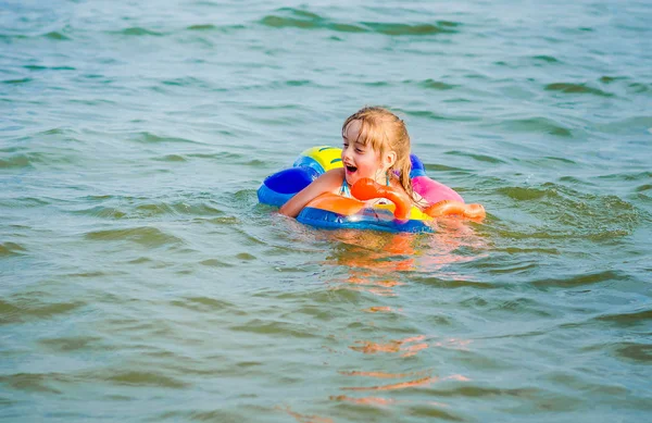 Έξι ετών κορίτσι κολυμπάει στη θάλασσα κάθισε στο δαχτυλίδι καουτσούκ, κολύμπι και ευτυχισμένα χαμόγελα. — Φωτογραφία Αρχείου