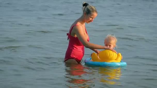 Tre-årig pige svømmer i havet sad på gummiringen med sin mor . – Stock-video