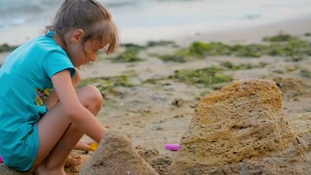 Zesjarige meisje bouwt een zandkasteel op het strand in de buurt van de zee. — Stockvideo