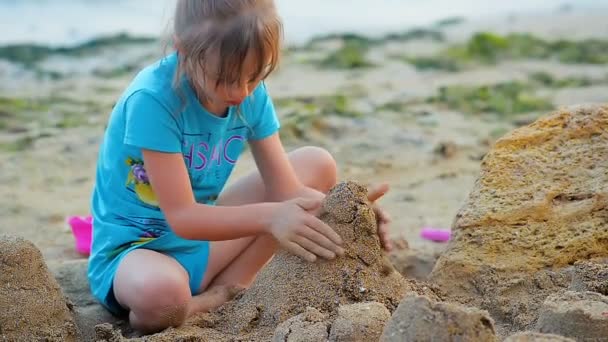 Primer plano una niña de seis años construye un castillo de arena en la playa en la costa del mar . — Vídeo de stock