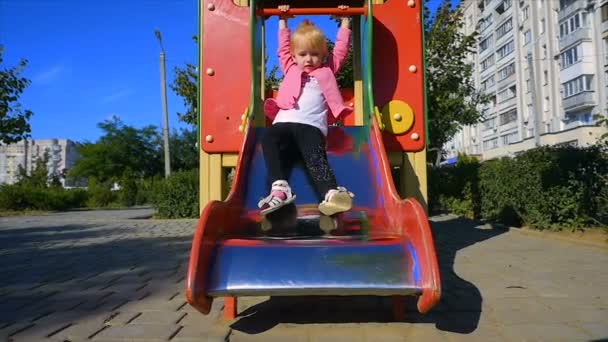 Медленное движение: девушка трех лет спускается с горки на детской площадке . — стоковое видео