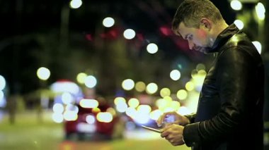 Genç adam otuz bir deri ceketli bir tablet ile bir gece şehirde duruyor.