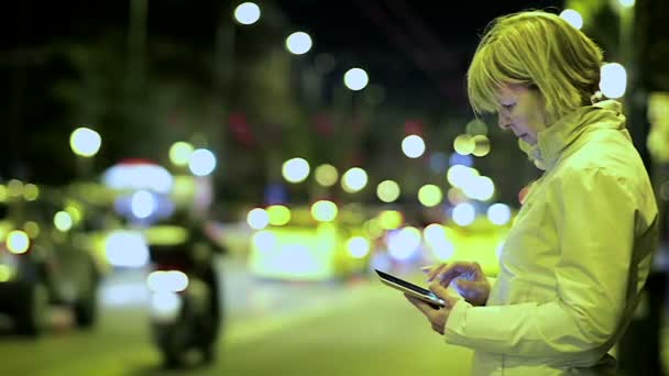 Vrouw van vijftig in een leren jas is permanent in een stad van de nacht met een tablet. — Stockvideo