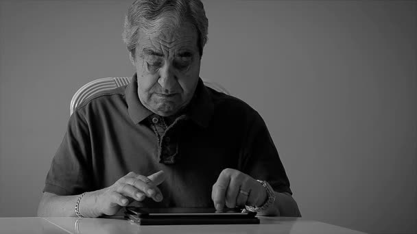Пожилой человек семидесяти лет печатает электронную почту на планшете дома в монохромном . — стоковое видео