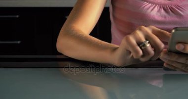 Bir genç kızın yakın çekim masada oturur ve evde mutfakta smartphone okuyun.