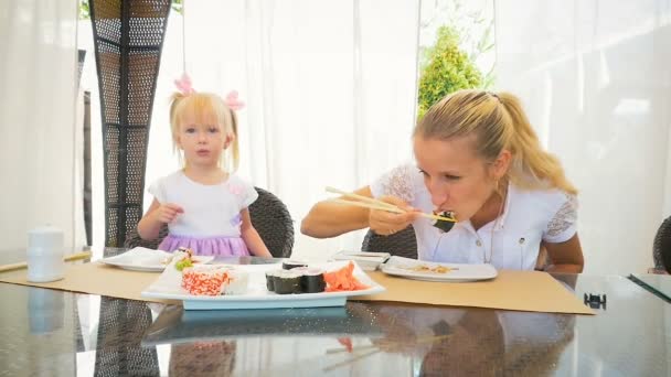 Maman et sa fille mangent des sushis avec des baguettes dans un restaurant d'été . — Video