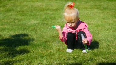 Ağır çekim: küçük kız üç-yıl çimenlerin üzerine oturmuş ve sabun köpüğü üfleme.