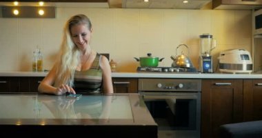 Dolly sevimli bir kız güneşli bir günde mutfak bir masada oturur ve akıllı telefon üzerinde bir ileti yazar.