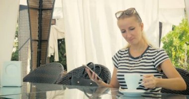 Genç kız bir yaz kafede otururken, lezzetli kahve içme ve telefonda bir mesaj yazma.