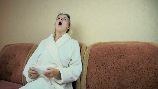 Slowmotion: ung flicka i en hem morgonrock nyser och våtservetter hans näsa med en näsduk på soffan. — Stockvideo