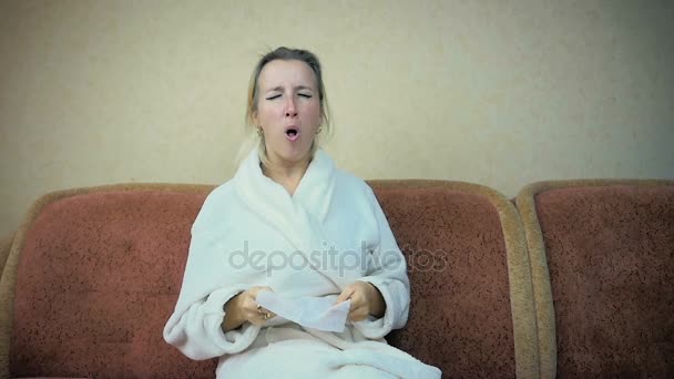 Movimiento lento: chica joven en un vestido de casa tose y estornuda sentado en casa en el sofá . — Vídeo de stock