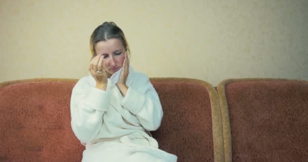 Jeune fille dans une robe de chambre à la maison tousse et éternue assis à la maison sur le canapé . — Video