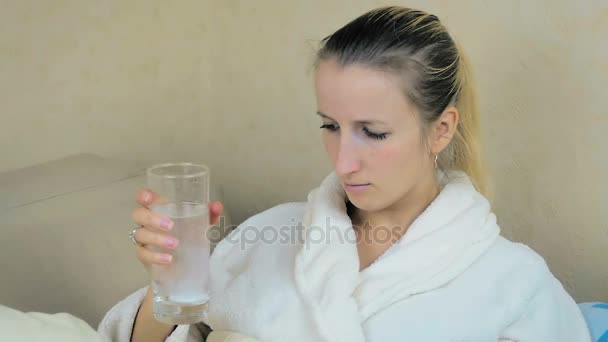 Slowmotion: sjuk ung flicka i en hem dressing dricker en brustablett med aspirin på soffan. — Stockvideo