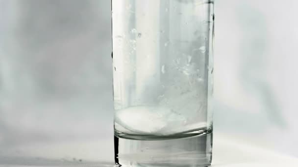Movimiento lento: en un vaso de agua, dos tabletas efervescentes de aspirina caen y se disuelven en agua . — Vídeo de stock