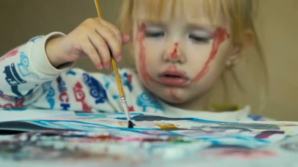 Nahaufnahme eines hübschen dreijährigen Mädchens, das zu Hause am Tisch in ein Album malt. — Stockvideo