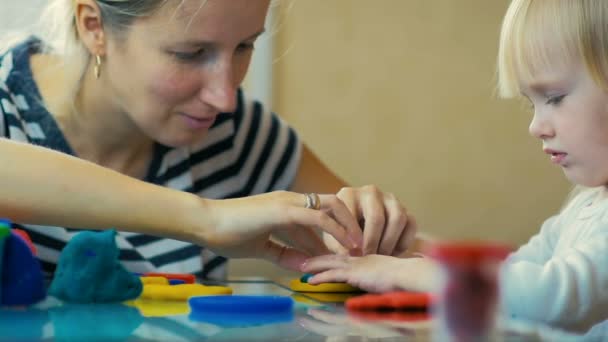 LOW MOTION: close-up uma mãe ensina sua filha de três anos de idade a esculpir estatuetas de plasticina em casa . — Vídeo de Stock