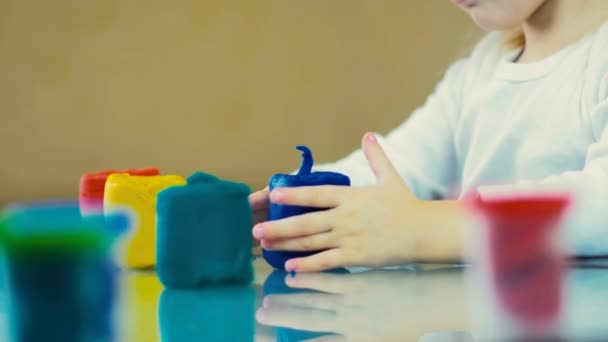 SLOW MOTION: Primo piano una bambina di tre anni tiene plastilina e scolpisce statuette a casa . — Video Stock