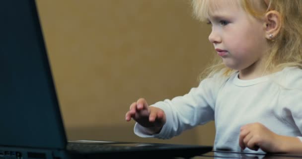 Närbild en liten flicka på tre år gamla självständigt inkluderar tecknad film på en bärbar dator och titta på skärmen hemma. — Stockvideo