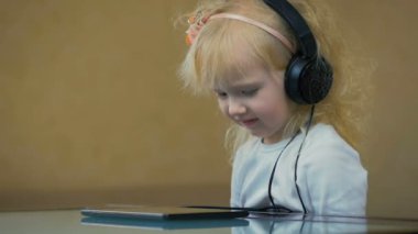 Ağır çekim: Yakın çekim üç-yıl-yaşlı büyük kulaklıklar müzik Internet tablet üzerinde küçük bir kız.