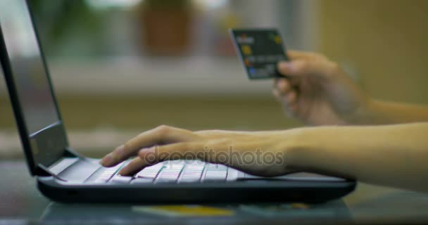 Gros plan d'une main féminine détient une carte de crédit et entre le numéro de la carte de crédit. Fait des achats sur la boutique en ligne en utilisant un ordinateur portable . — Video