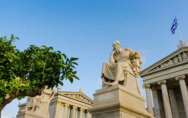 Ancient statue of the great Greek philosopher Socrates on background classical columns and the Greek flag.