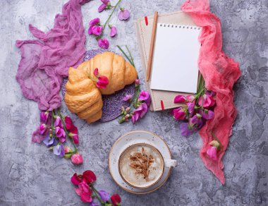 Kahve, kruvasan, çiçek ve defter.
