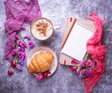 Kahve, kruvasan, çiçek ve defter.