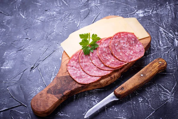 Sliced cheese and salami on wooden board
