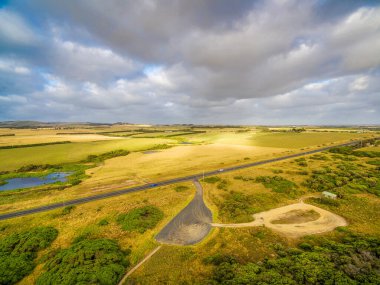 Avustralya 'da gün batımında çayırların ve otlakların arasından düz kırsal yol - hava manzarası