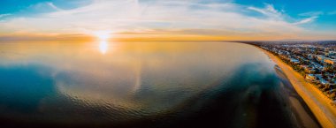 Güneşin soluk kesen manzarası bulutların yansımasıyla pürüzsüz su yüzeyinde batıyor.