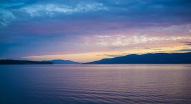 Tazmanya, Avustralya 'da tepelerde pembe ve turuncu gün batımı ve su.