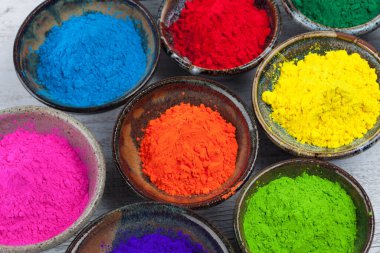 Beyaz ahşap masa üzerinde canlı Holi renkli pudralı seramik kaseler.