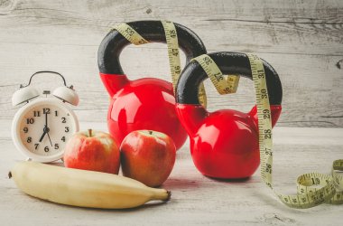 Kırsal beyaz ahşap masa üzerinde mezuralı, elmalı, muzlu ve antika saatli iki kırmızı çaydanlık. Sağlıklı beslenme ve spor konsepti.