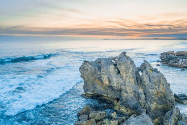Gün batımında okyanus dalgaları kayaların üzerinde eziliyor.