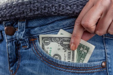 Kadın eli kot pantolonun cebinde 1 dolarlık banknota uzanıyor. Yakın plan. Asgari ücret ve kötü ekonomi konsepti.