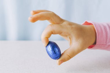 Çocuğun elinde çikolatalı Paskalya yumurtası var. Mavi folyoya sarılı. İki parmağında da kopya alanı var.